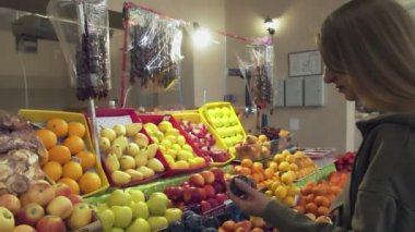 Genç bir kadın marketteki raflardan erik seçiyor.