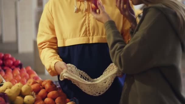Молодая пара выбирает персики и кладет их в веревочный мешок на рынке — стоковое видео