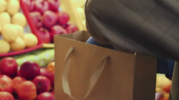 Detailní záběr ženy v modrých rukavicích dává červená jablka do papírové tašky na trhu — Stock video