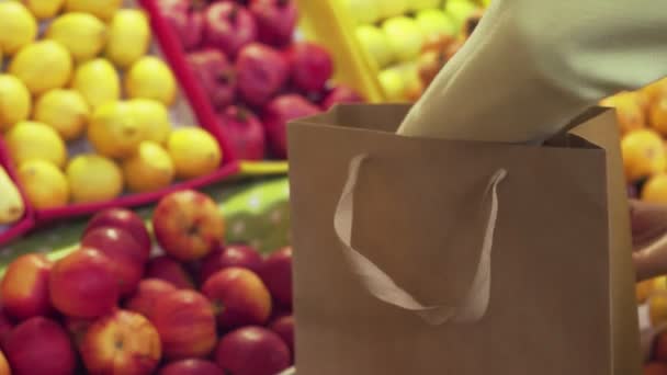 Gros plan de la femme en manteau jaune met des pommes rouges dans un sac en papier au marché — Video