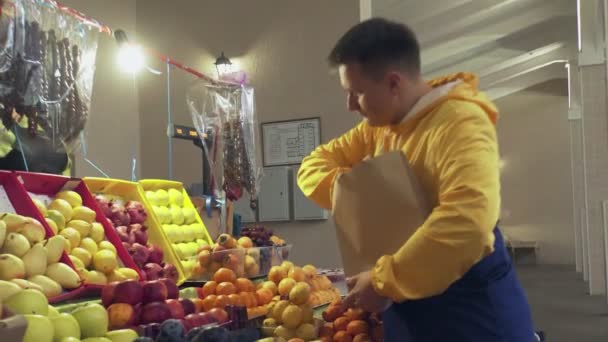 Мужчина выбирает свежие мандарины, кладет их в бумажный пакет, который Анг отдает продавцу на рынке. — стоковое видео
