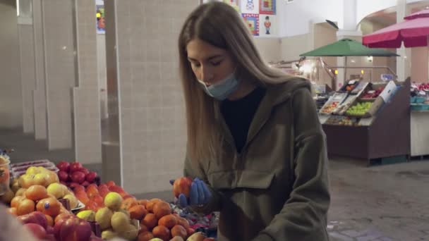 Νεαρή γυναίκα με προστατευτική μάσκα και μπλε γάντια μυρίζει και επιλέγει ροδάκινα στα ράφια των καταστημάτων στην αγορά — Αρχείο Βίντεο