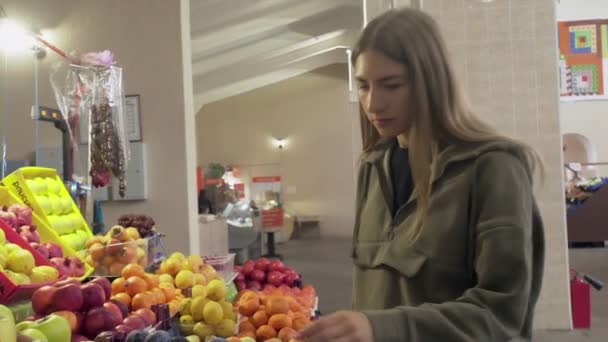 Mujer joven huele y elige ciruelas en los estantes de la tienda en el mercado — Vídeos de Stock