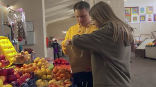 Młoda para wybiera wiele różnych owoców i je do papierowej torby na rynku — Wideo stockowe