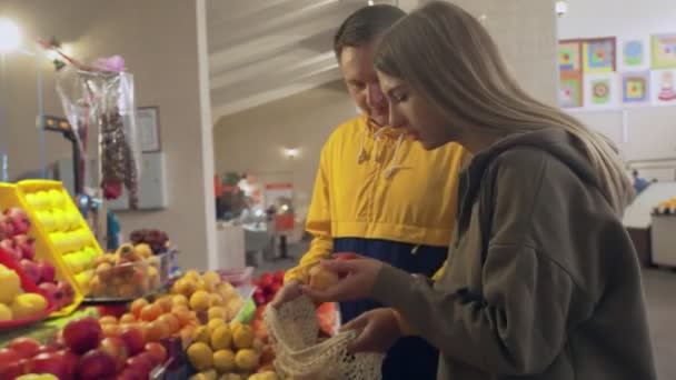 Giovane coppia sceglie alcune pesche e li mette in una borsa stringa al mercato — Video Stock