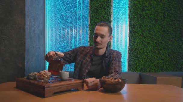 Молодой человек пьет традиционный китайский чай, наливает горячий чай из чайника в чашку и пьет его в кафе — стоковое видео