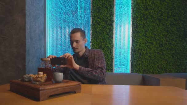 Молодой человек фотографирует традиционный китайский чай в кафе — стоковое видео