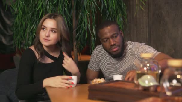 Dos amigos hombre africano y mujer caucásica bebe té chino y come galletas en la cafetería tradicional — Vídeo de stock