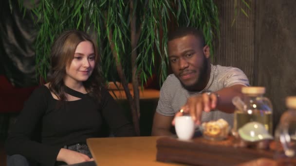 Dos de los mejores amigos hombre africano y mujer caucásica bebe té chino y come galletas en la cafetería tradicional — Vídeos de Stock