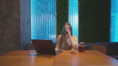 Genç kadın defter üzerinde çalışmayı bitirdi ve kafede telefon kullanmaya başladı.