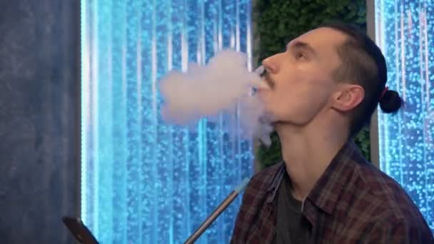Primo piano dell'uomo che fuma la tradizionale pipa narghilè e fa nuvole di fumo in forma di anelli. — Video Stock