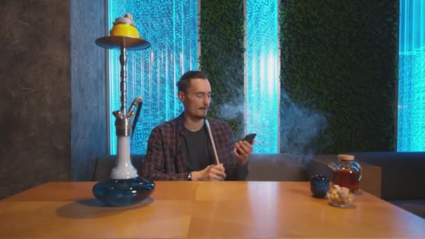 Mladý muž mluví po telefonu a kouří shisha v hookah kavárně — Stock video