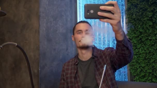 Atractivo hombre alegre se toma una selfie en el teléfono mientras fuma una shisha — Vídeos de Stock