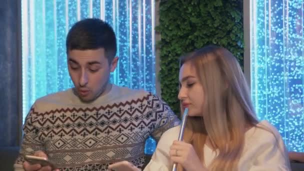 Detailní záběr mladého páru relaxovat v salonku Shisha hookah bar. Používají telefony a kouří hookah. — Stock video