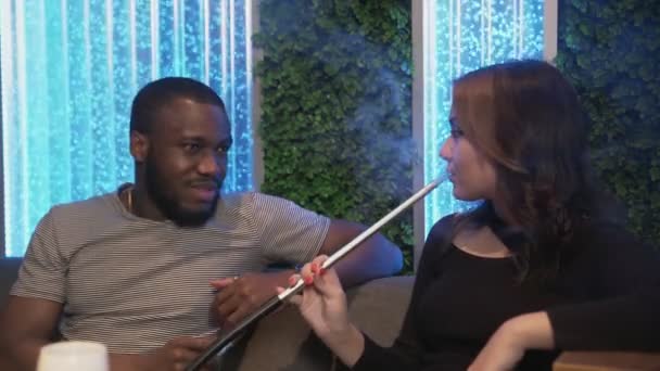 Jeune homme africain parle avec femme caucasienne pendant qu'elle fume narguilé — Video