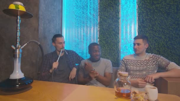 Des amis multinationaux de la société s'assoient au bar Shisha, fument et discutent — Video