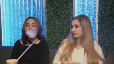 Nargile barında iki bayan arkadaş. Bir kadın sigara içmeyi teklif ediyor, diğeri reddediyor.