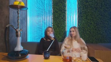 Nargile barında iki bayan arkadaş. Bir kadın sigara içmeyi teklif ediyor, diğeri reddediyor ve çay içiyor.