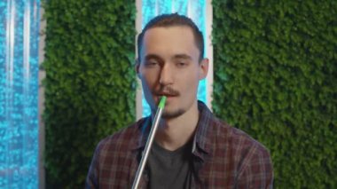 Genç yakışıklı adam nargile içiyor ve kameraya bakıyor.