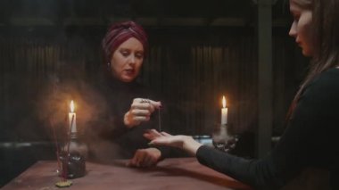 Kıdemli kadın falcı, geleceği genç müşterisine anlatmak için iplikle iğne kullanıyor.