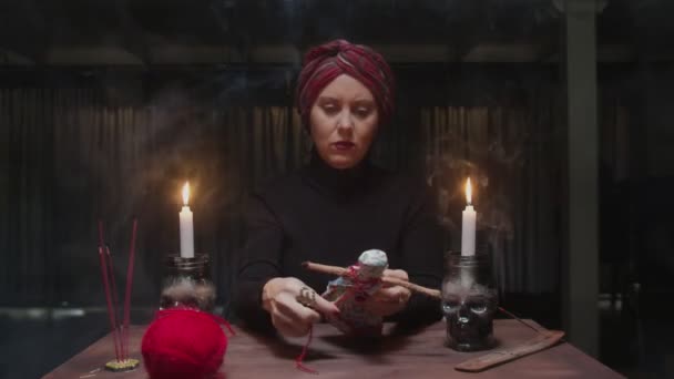 Старшая ведьма-гадалка вонзает иглу в куклу вуду в ужасном магическом ритуале — стоковое видео