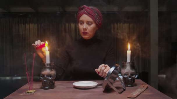 Senior häxa kvinna spåman håller spegel i ena handen och tänder rött ljus och droppande vax i en tallrik i fruktansvärd magi ritual — Stockvideo
