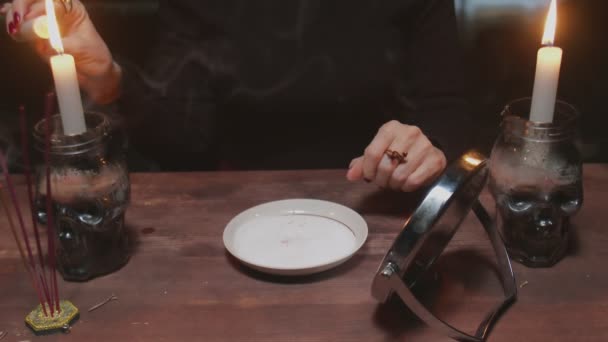 Senior donna strega indovino tiene specchio in una mano e accende candela rossa e cera gocciolante in un piatto in terribile rituale magico — Video Stock