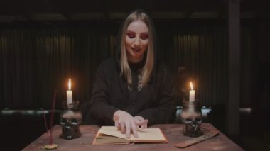 Genç cadı kadın falcı karanlık ofisinde sihirli kitap okuyor.