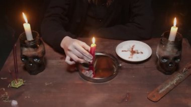 Genç cadı kadın falcıya yaklaş. Masadaki aynaya bak ve elinde mum tut. Korkunç bir büyü ayiniyle bir tabağa mum damlatıyor.