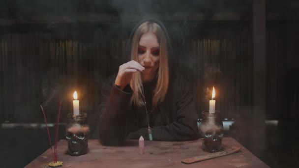 Молодая ведьма-гадалка вращает голубой магический кристалл вокруг другого кристалла на столе в мистическом ритуале — стоковое видео