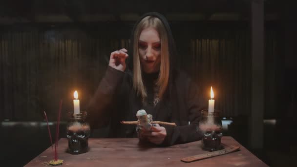 Young witch female fortune teller sticks a needle into voodoo doll in terrible magic ritual — Stock Video
