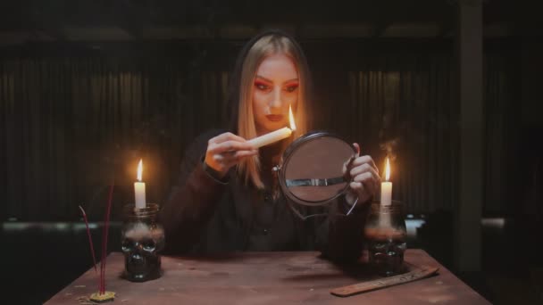 Молодая ведьма-гадалка держит свечу в одной и смотрит в зеркало в ужасном магическом ритуале — стоковое видео