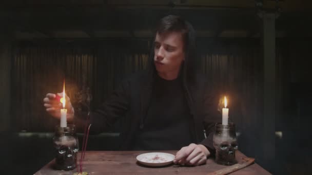 Concentrado misterioso mago adivino macho enciende una vela roja, duro lo pone en plato en ritual mágico — Vídeo de stock