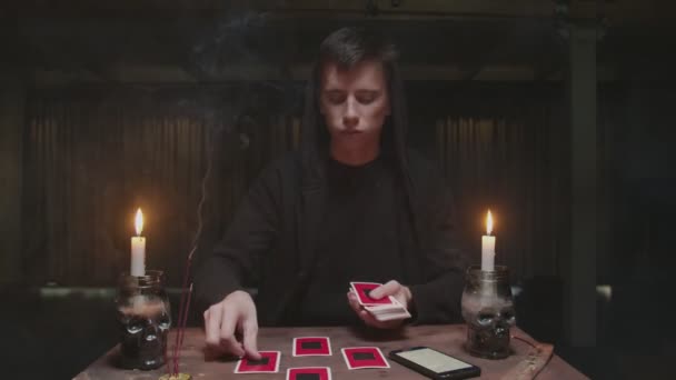 Asistente misterioso concentrado adivino masculino utiliza la tarjeta del tarot y el teléfono para leer el futuro — Vídeos de Stock