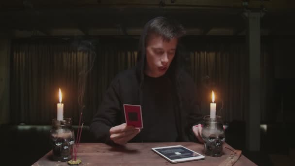 Geconcentreerde mysterieuze tovenaar mannelijke waarzegster gebruikt tarot kaart en tablet om de toekomst te lezen — Stockvideo