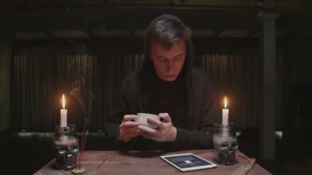 Concentré mystérieux magicien diseur de bonne aventure masculine tient tasse de café et regarde tablette à la lecture du destin — Video