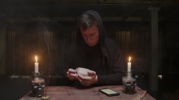 Concentrado misterioso mago adivino masculino está sosteniendo taza de café y mira el teléfono para leer el destino — Vídeo de stock