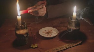 Gizemli büyücü erkek falcıya yakın, kırmızı bir mum yakar, onu tabağa koyar ve sihirli bir kristal kristali döndürür.