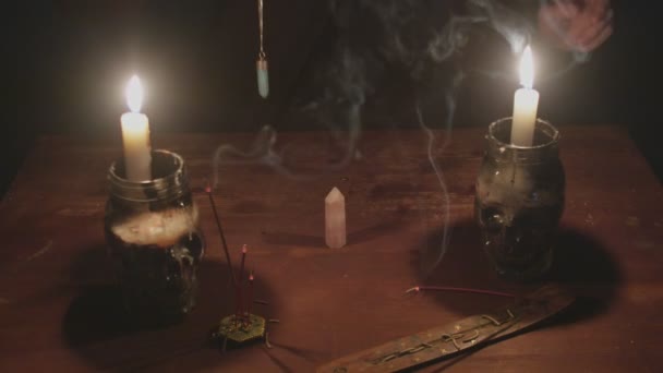 Крупним планом таємничий чарівник чоловічої статі обертає блакитний магічний кристал навколо іншого кристала на столі в містичному ритуалі — стокове відео