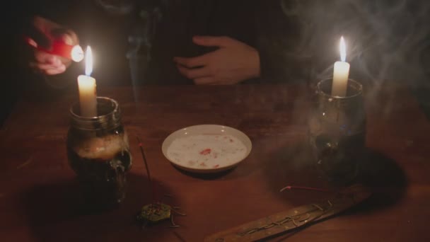 Närbild av mystiska trollkarl manliga spåman tänder ett rött ljus och sätter det på tallriken i magi ritual — Stockvideo