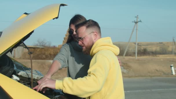 Молодий чоловік показує свою дівчину, як перевірити двигун у своєму фургоні Кемпер у дорожній поїздці — стокове відео