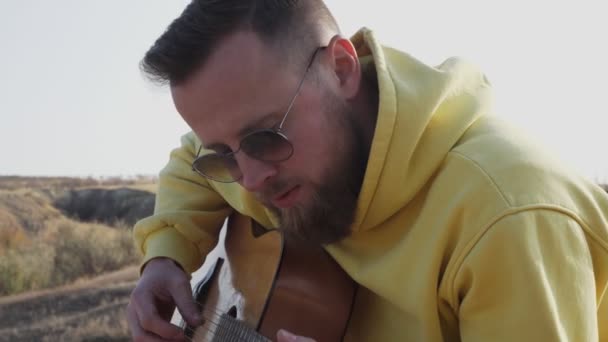 Mladý hipster vousatý muž v slunečních brýlích hrát kytaru venku na táboření — Stock video