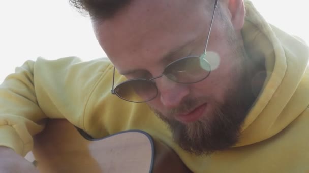 Młody hipster brodaty mężczyzna w okularach przeciwsłonecznych grać na gitarze na zewnątrz na kempingu — Wideo stockowe