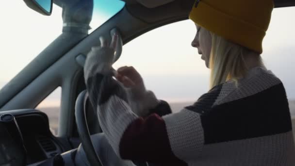 Młoda kobieta w żółtym kapeluszu siedzi w samochodzie i pozuje przed kamerą — Wideo stockowe