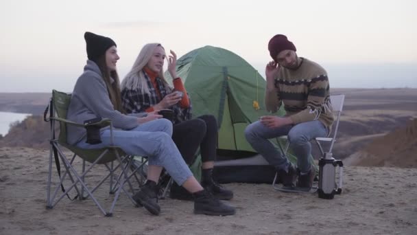 Jeunes amis heureux campeurs assis près de la tente et la voiture, boit un thé chaud et parle — Video