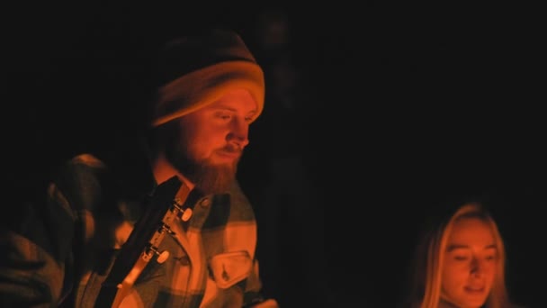 Barbu campeur homme dans chapeau regarde sur le feu de joie la nuit — Video