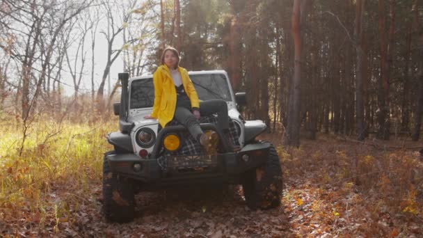 Jovem mulher feliz em casaco amarelo senta-se no carro e posa — Vídeo de Stock