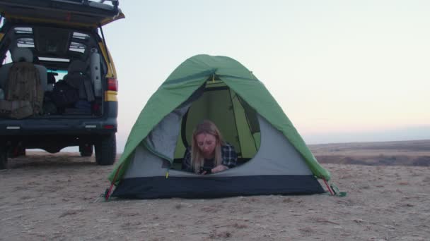 Jonge vrouw ligt in de tent en maakt gebruik van telefoon op de berg — Stockvideo