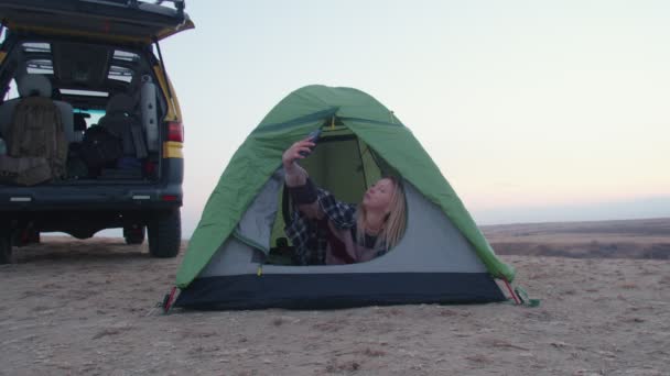 Jeune femme se couche dans la tente et prend selfie au téléphone sur la montagne — Video