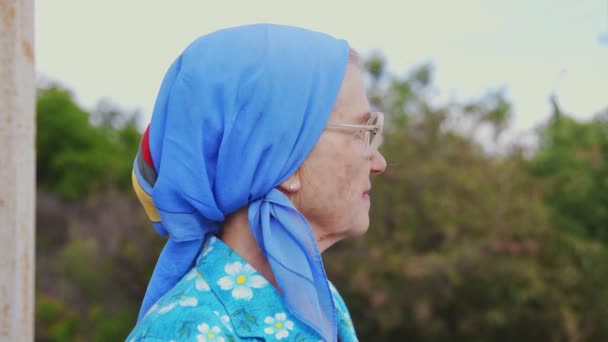 Nahaufnahme einer alten Seniorin in Blau an der Bushaltestelle, die auf den Bus wartet — Stockvideo